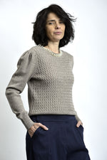 Vedere laterală a puloverului cu torsade și colier decorativ cu perle, evidențiind textura tricotului.