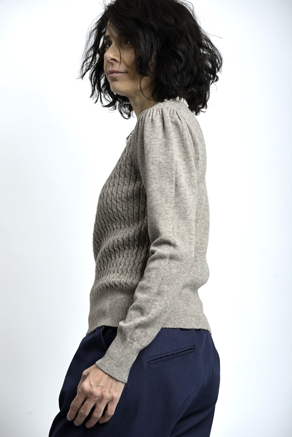 Vedere laterală a puloverului cu torsade și colier decorativ cu perle, evidențiind textura tricotului.