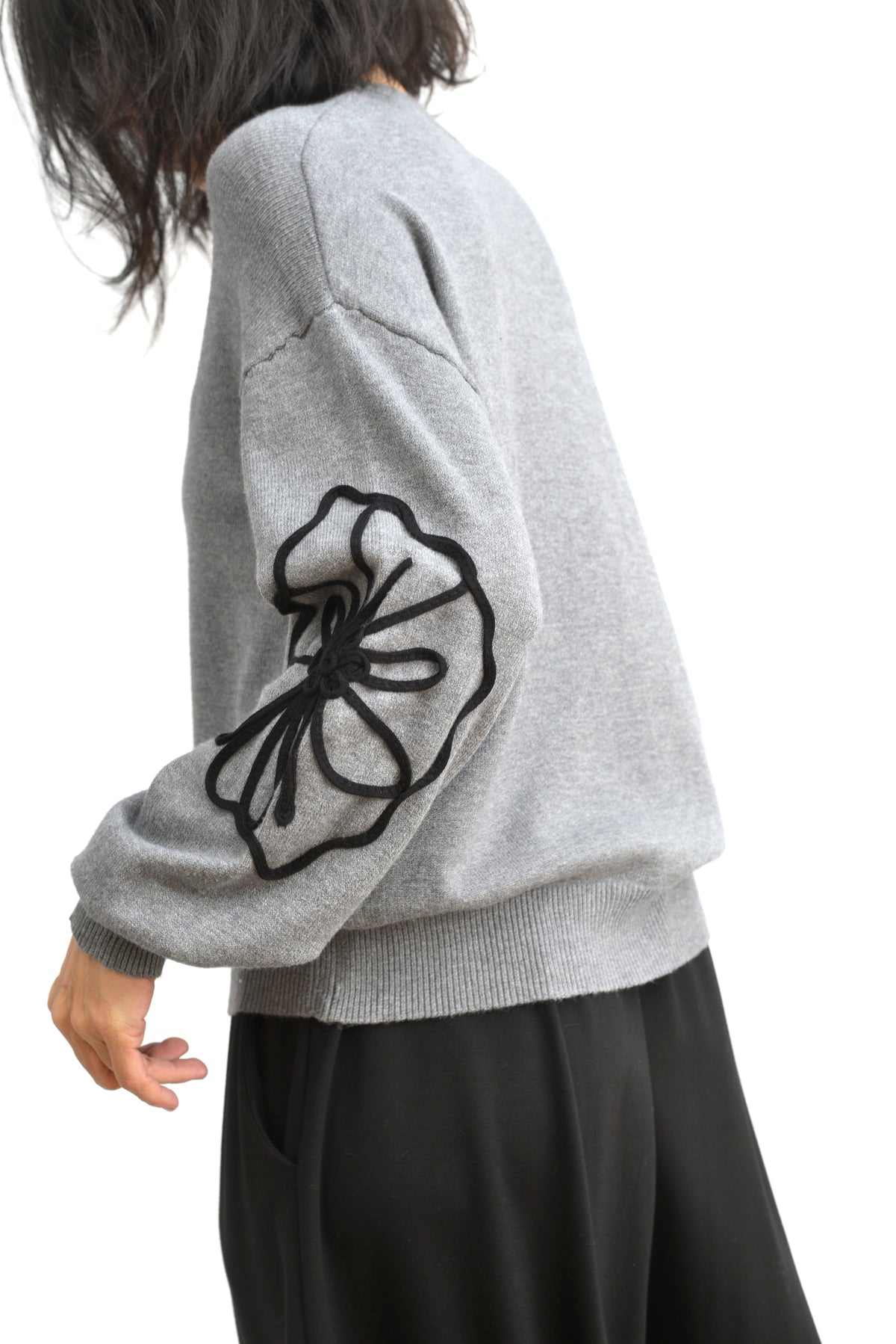 Pulover gri din tricot, cu floare mare din șnur pe lateral și mâneci lungi bufante.