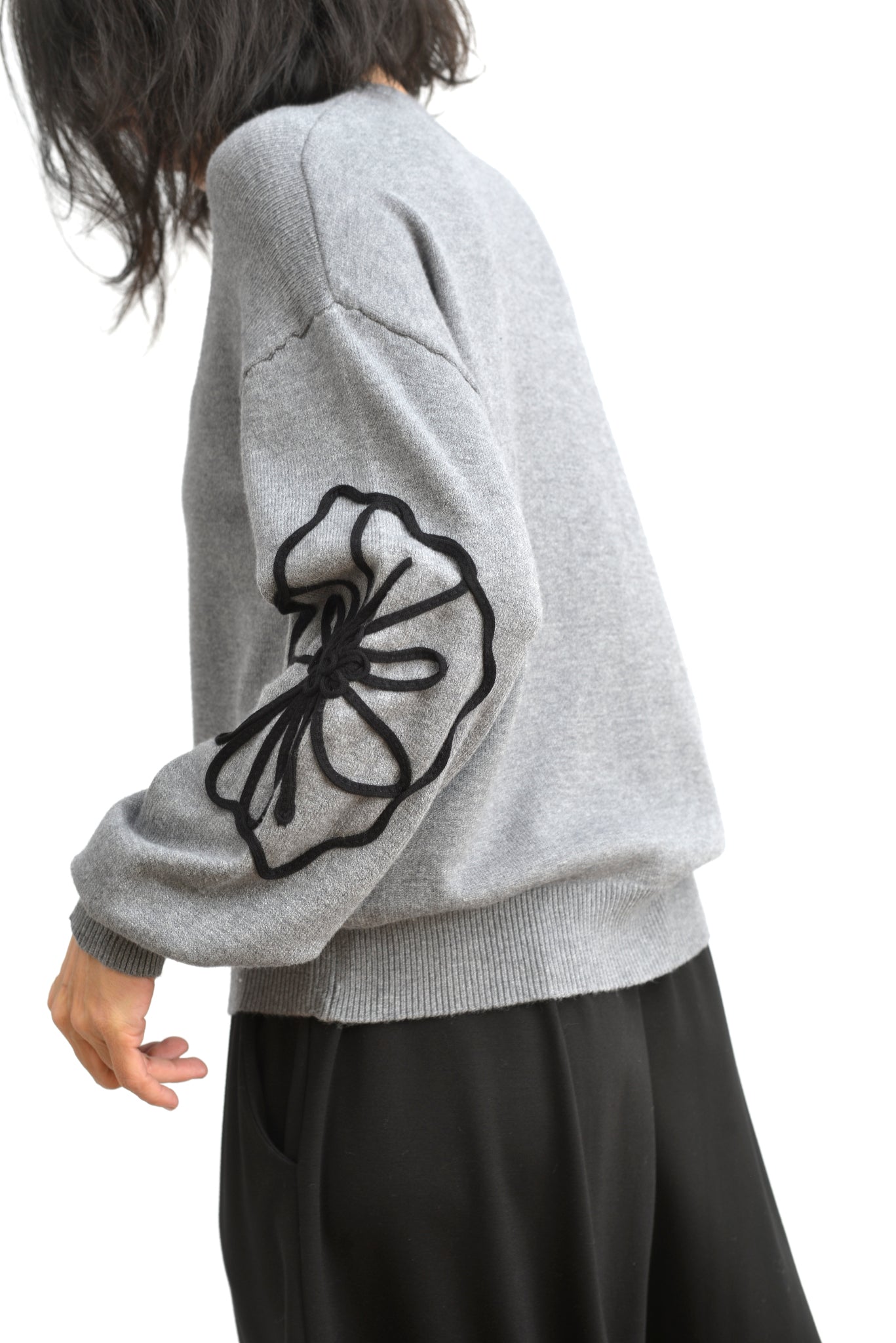 Pulover gri din tricot, cu floare mare din șnur pe lateral și mâneci lungi bufante.