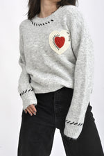 Pulover din tricot gri cu aplicație inimă macramé, fotografie semiprofil ce evidențiază textura materialului.