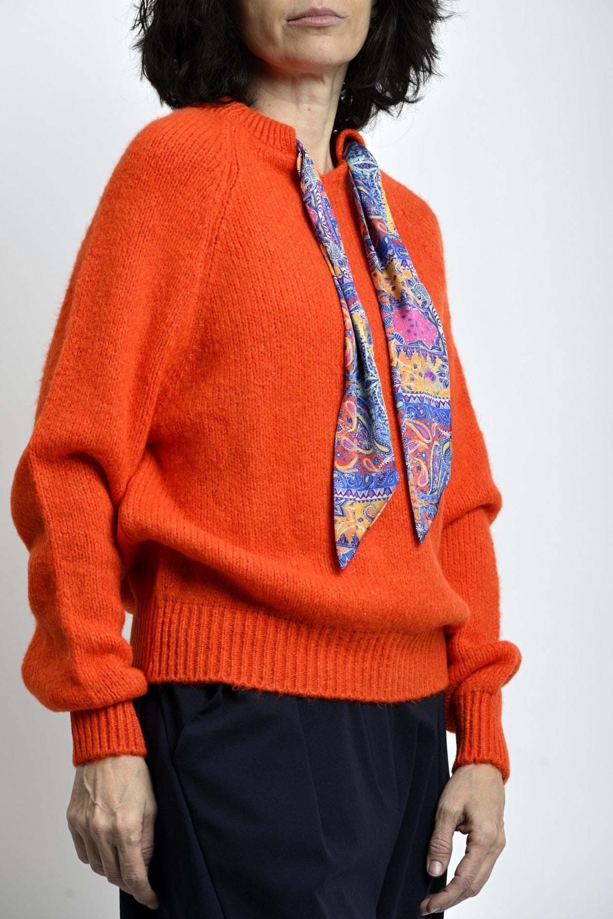 Pulover portocaliu din tricot moale, purtat cu eșarfă decorativă, stil casual-elegant.