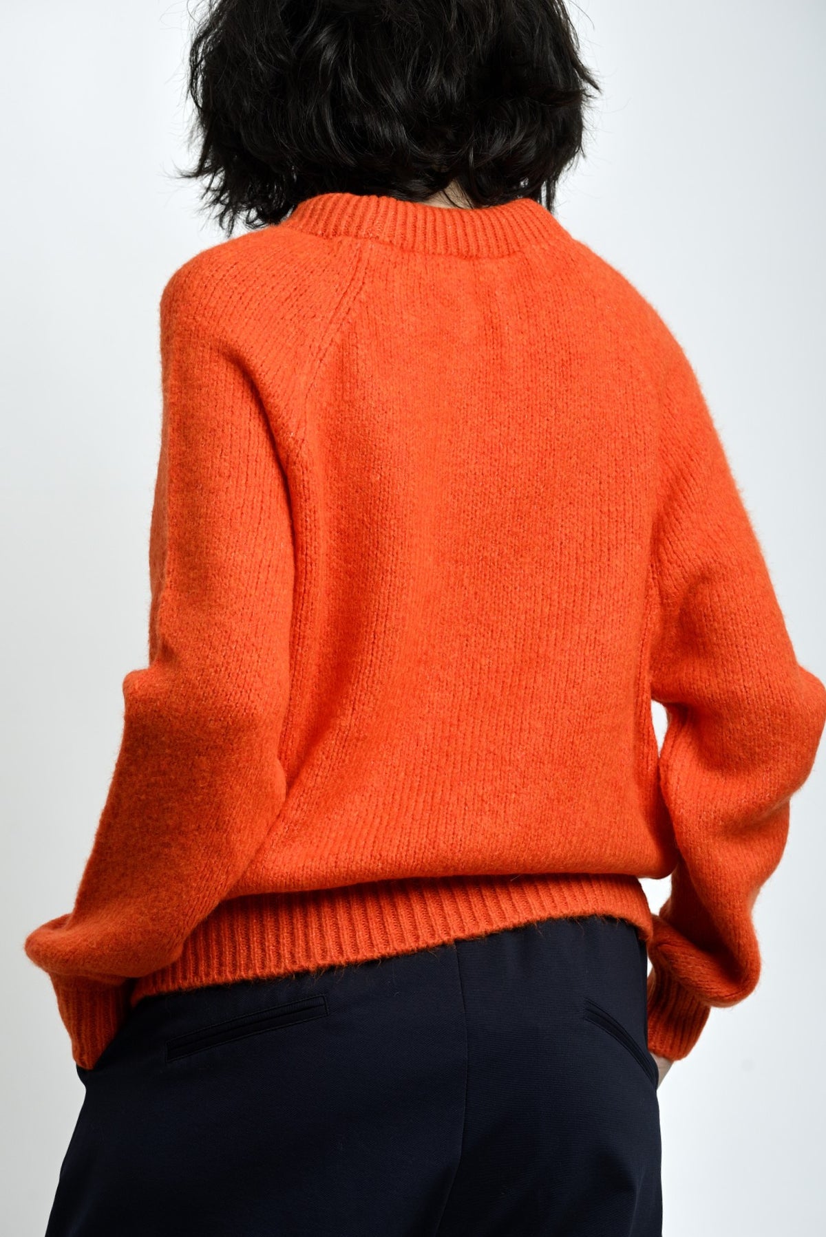 Vedere laterală pulover tricotat portocaliu, mâneci lungi și linie relaxată a corpului.