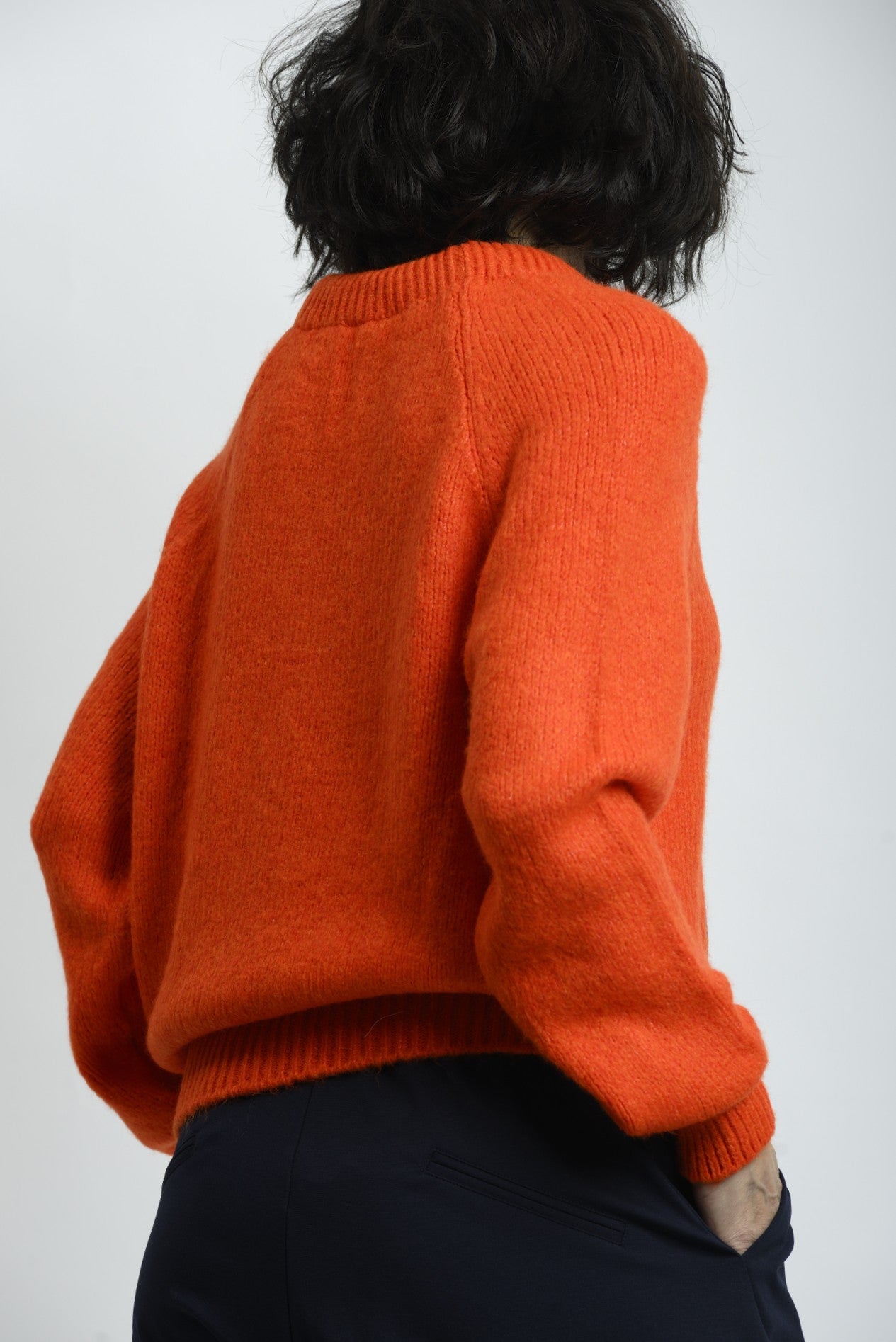 Pulover tricotat portocaliu, văzut din spate, cu croială lejeră și textură uniformă.