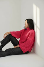 Vedere laterală pulover tricotat roz cu textură solzișori și croială lejeră.