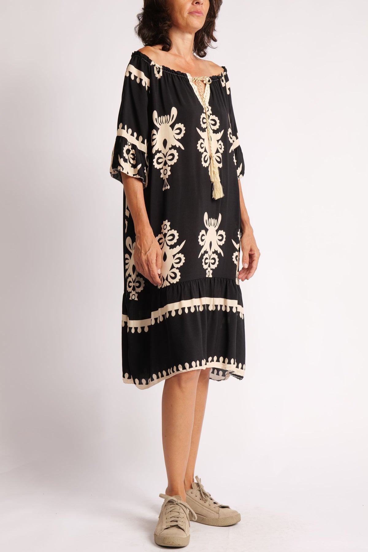 Rochie neagră boho, fotografiată lateral, cu mâneci trei sferturi și croială vaporoasă, decorată cu șnur auriu.