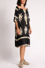 Rochie neagră boho, fotografiată lateral, cu mâneci trei sferturi și croială vaporoasă, decorată cu șnur auriu.