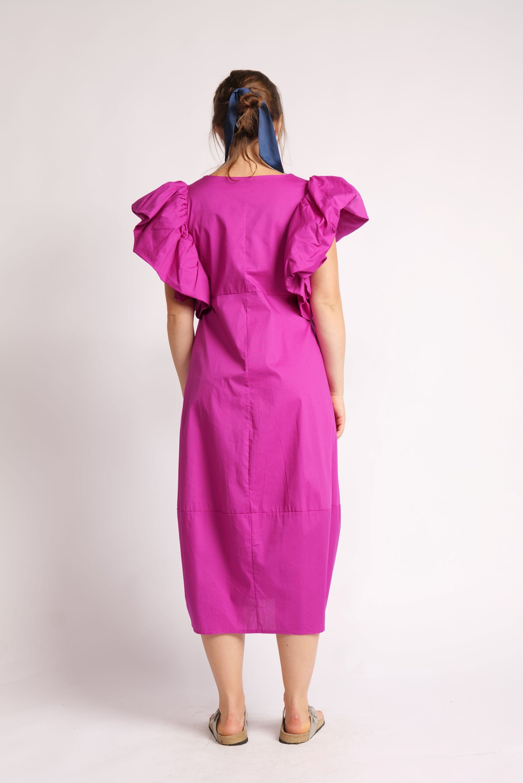 Rochie midi fucsia cu croială lejeră și mâneci bufante, purtată cu sandale.