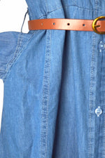Prim-plan cu talia rochiei lungi din denim, evidențiată de o curea subțire maro cu cataramă aurie.