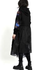 Detaliu de mânecă cu print artistic tip splash, pe fundal negru mat.