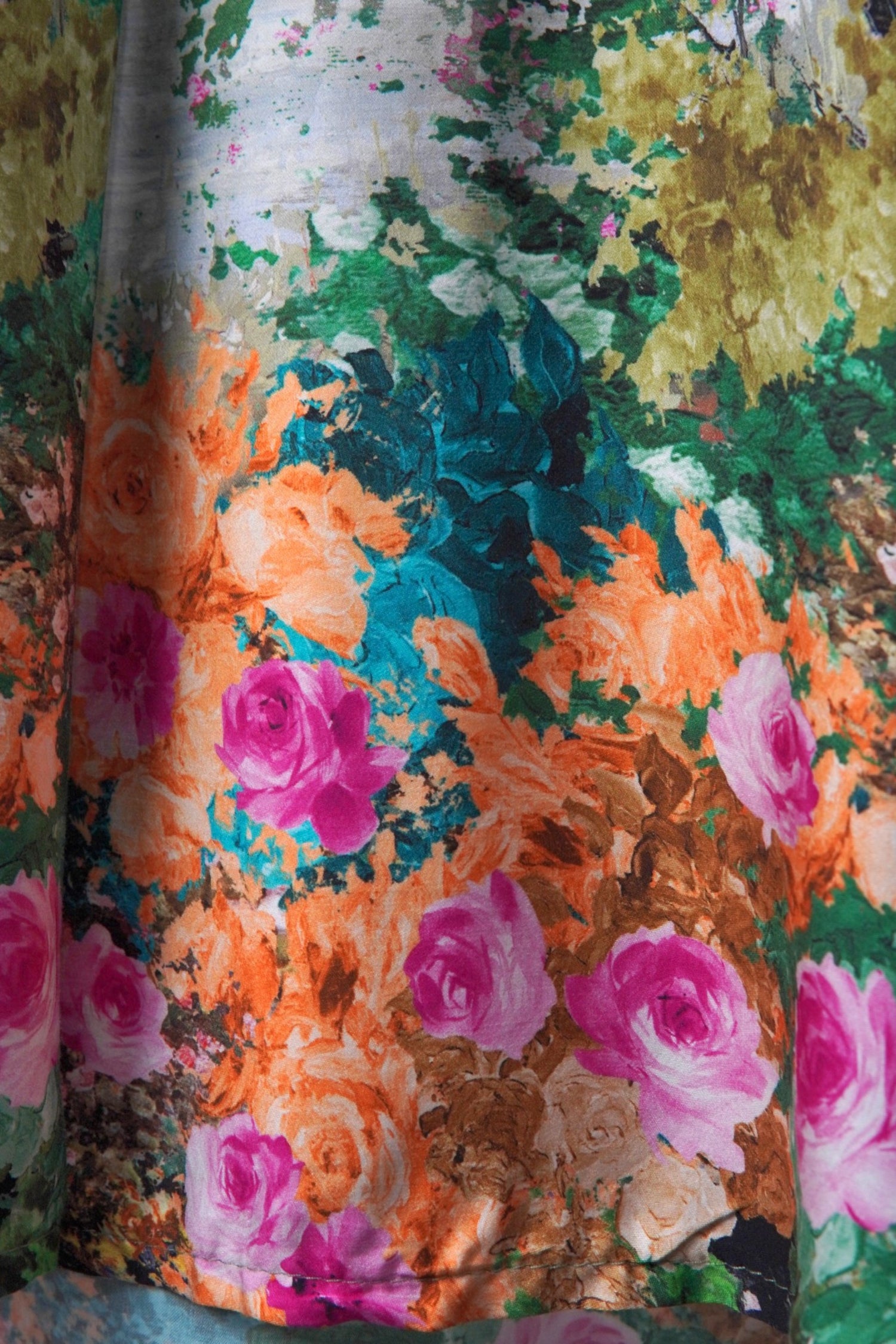 Detaliu al materialului unei rochii cu imprimeu floral, în nuanțe vibrante de roz, portocaliu și verde.
