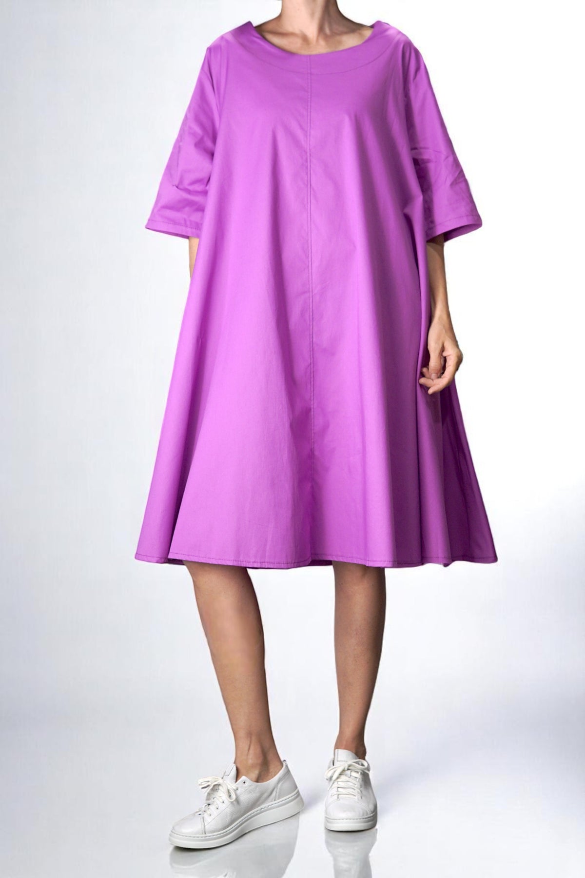 Rochie oversized din bumbac într-o nuanță vibrantă de cyclamen, cu croi în A, buzunare laterale și mâneci trei sferturi. Ținută relaxată, purtată cu adidași albi.