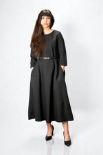 Rochie neagră lungă cu mâneci trei sferturi și centură subțire, design minimalist și buzunare laterale.

