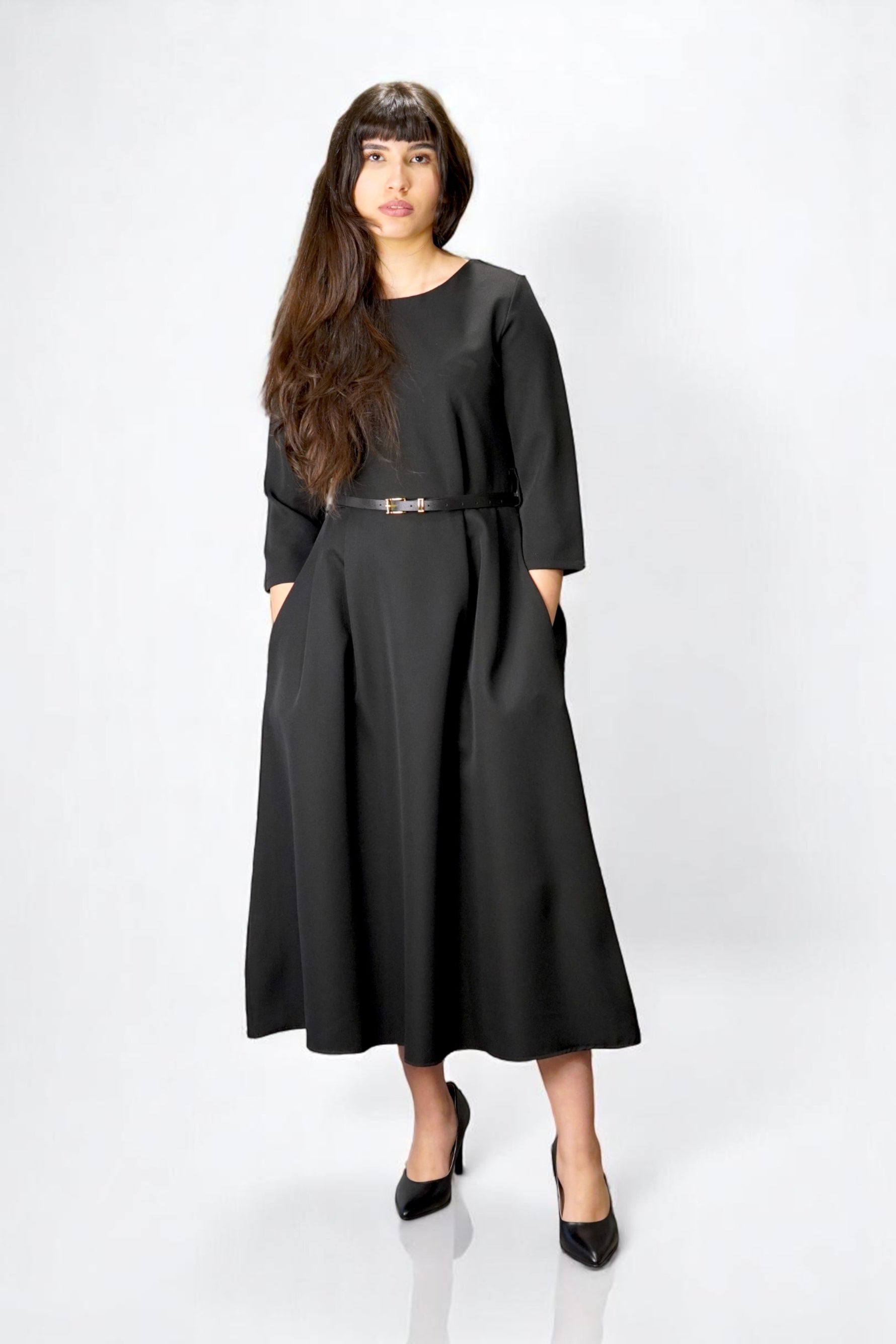 Rochie neagră lungă cu mâneci trei sferturi și centură subțire, design minimalist și buzunare laterale.

