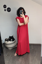 Rochie lungă roșie, vaporoasă, cu croială plisată și umeri lejeri, surprinsă într-un cadru de interior cu modelă în oglindă.