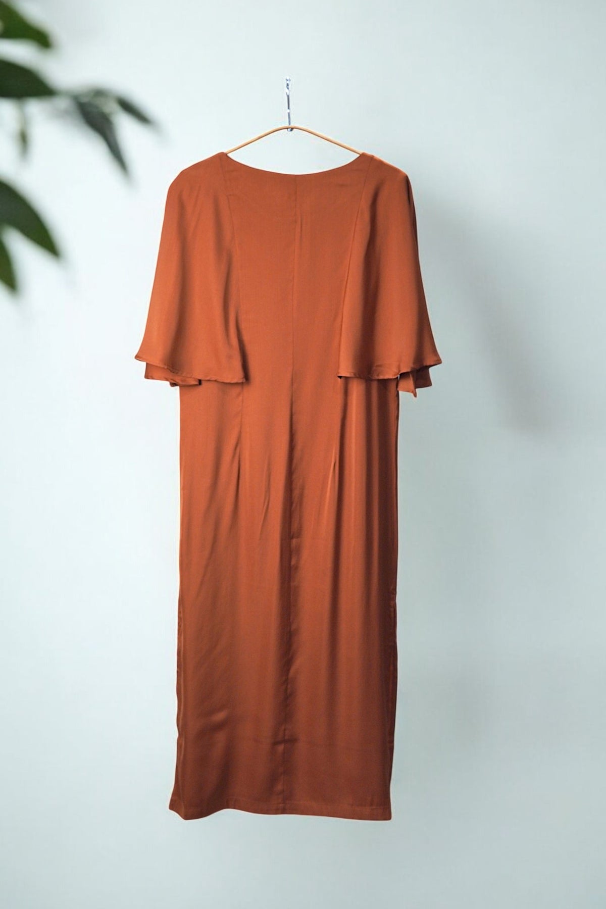 Rochie midi cărămizie cu mâneci fluture, văzută din spate, evidențiind croiala elegantă și fluiditatea materialului.