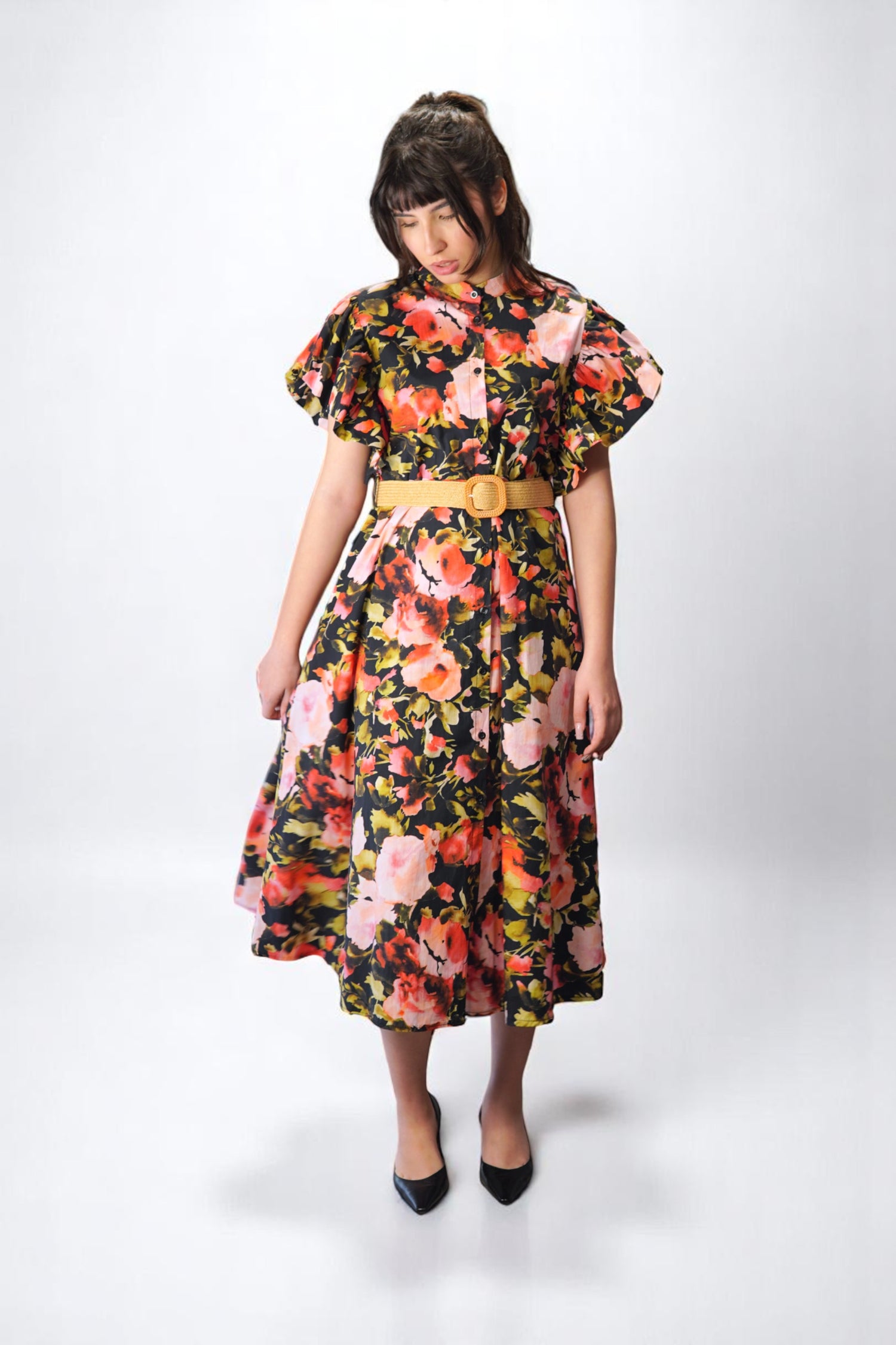 Rochie florală cu croi midi și volan dublu la umeri, evidențiată din lateral, accesorizată elegant.