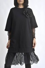 Rochie neagră oversize cu aplicație floare 3D pe umăr și dantelă la baza rochiei, evidențiind croiala lejeră.