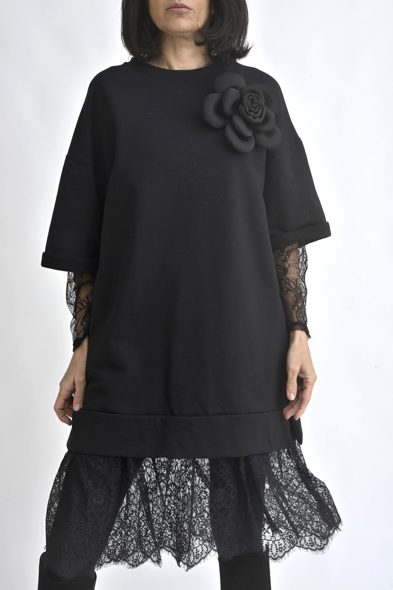 Rochie neagră oversize cu aplicație floare 3D pe umăr și dantelă la baza rochiei, evidențiind croiala lejeră.