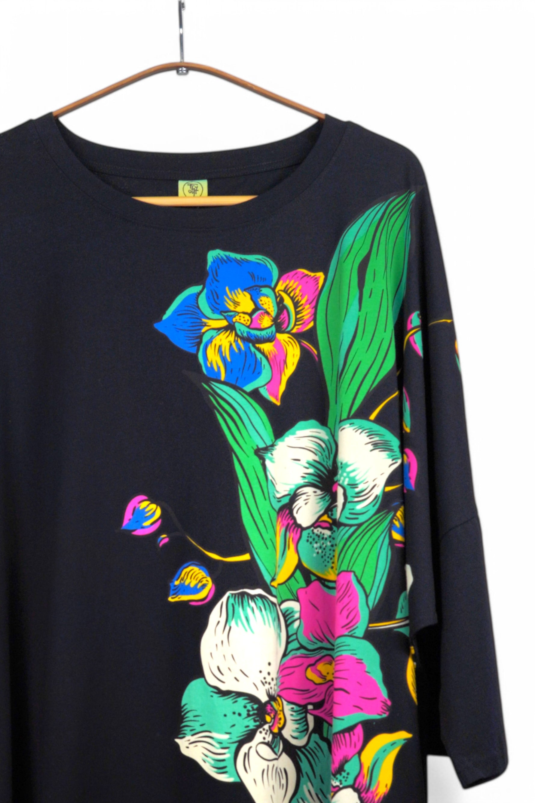 Detaliu imprimeu floral viu colorat pe partea superioară a unei rochii negre cu croială lejeră.