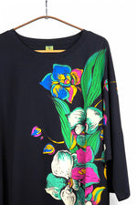 Detaliu imprimeu floral viu colorat pe partea superioară a unei rochii negre cu croială lejeră.