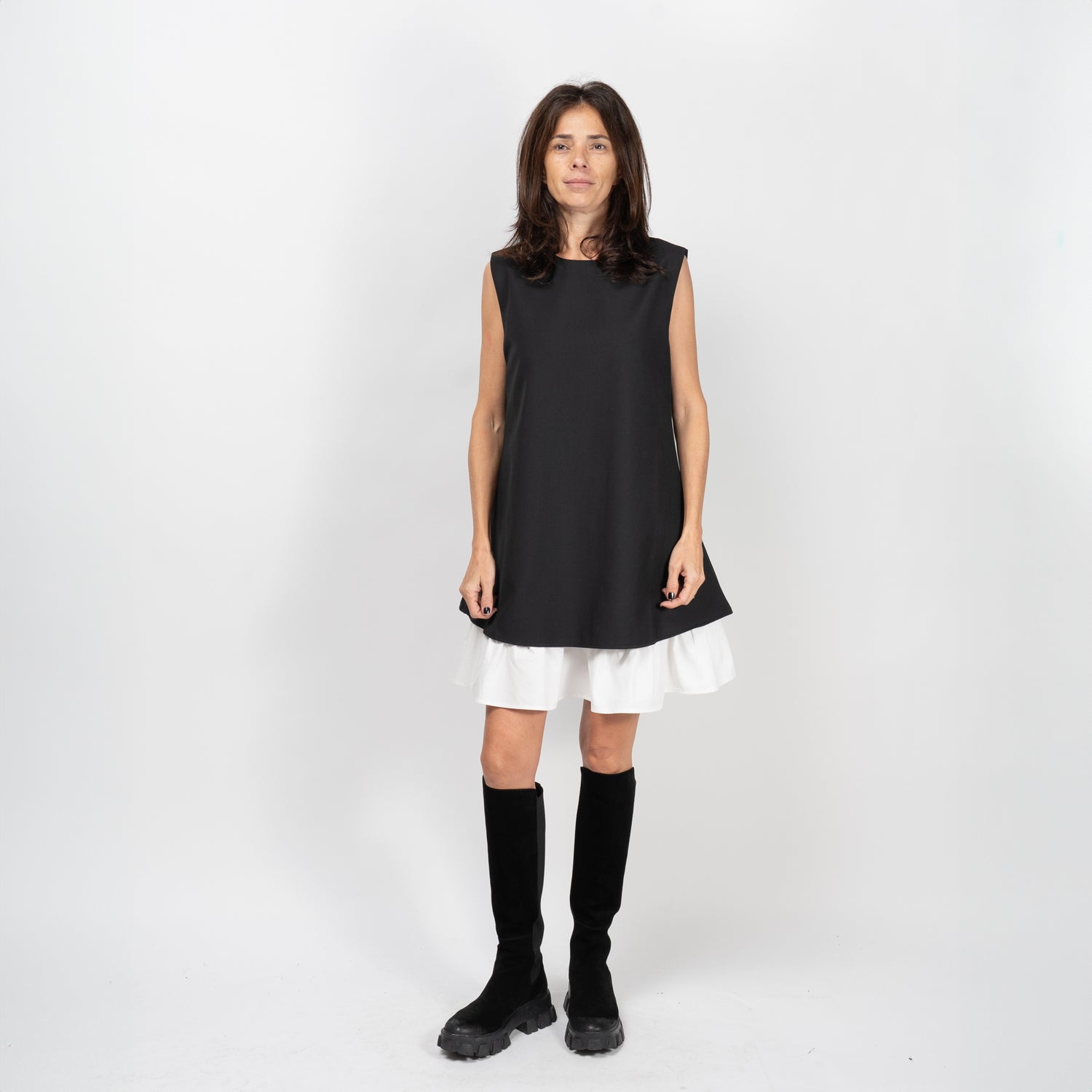 Model purtând o rochie neagră evazată cu volan alb, fără mâneci, în stil elegant și feminin.