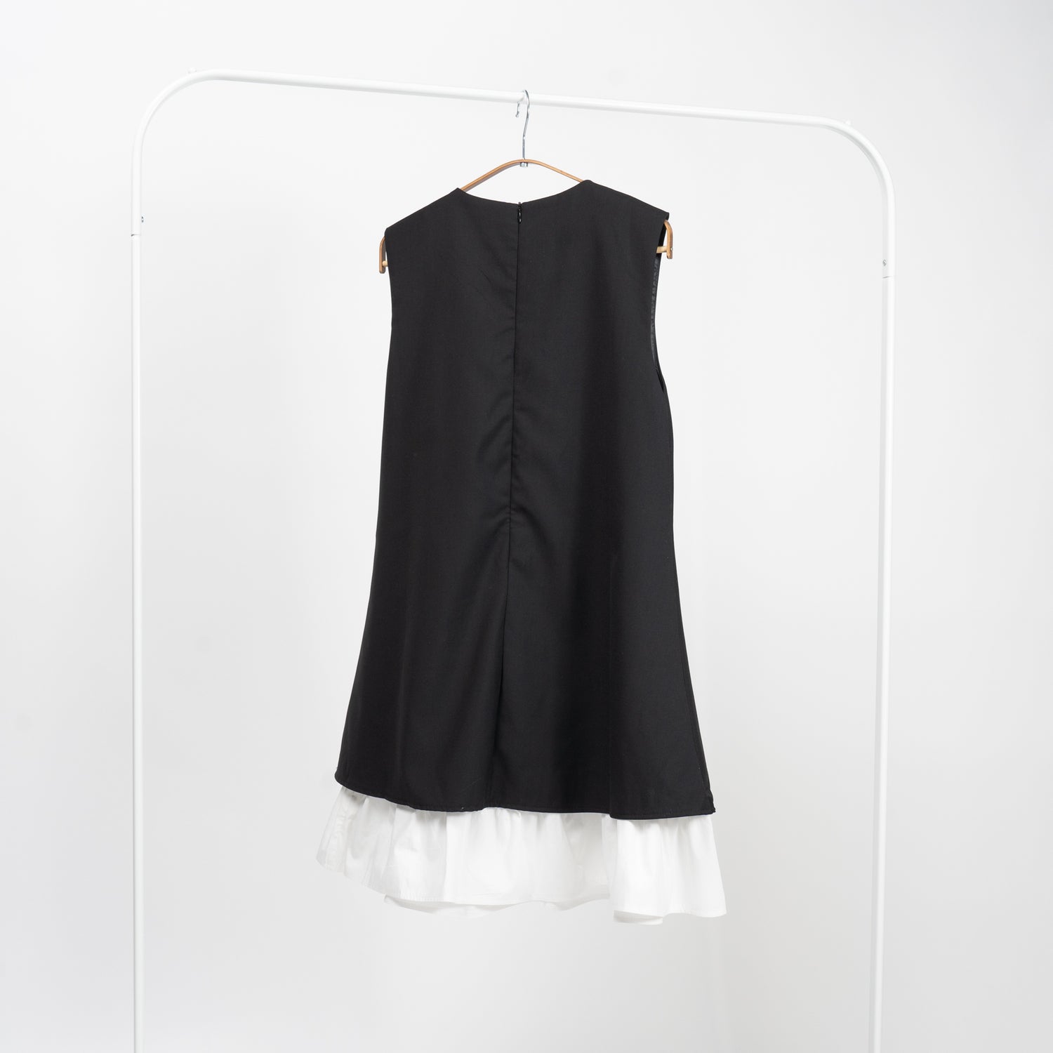 Spatele unei rochii negre elegante fără mâneci, cu detalii simple și volan alb la bază.