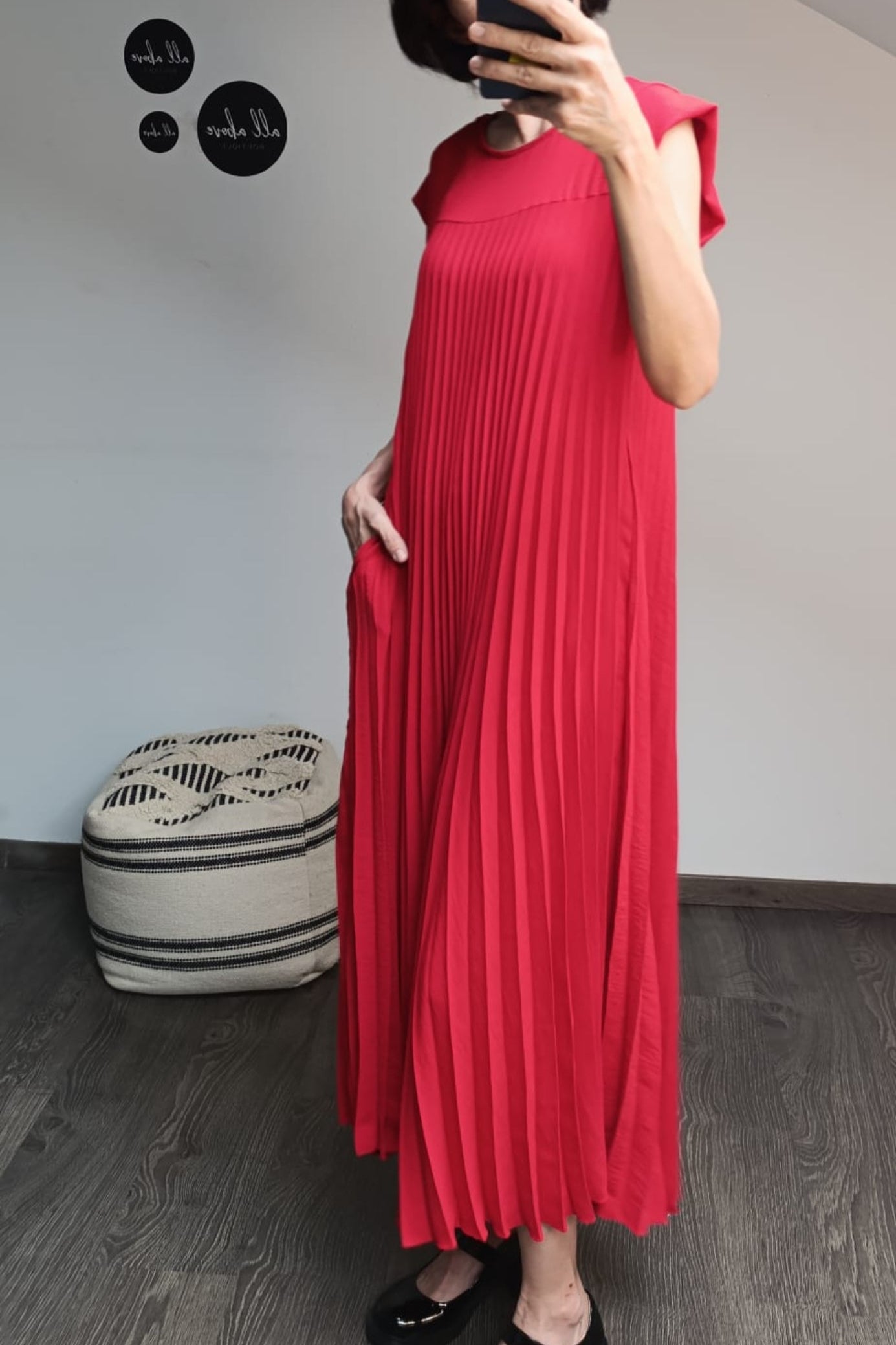Detaliu lateral al unei rochii roșii plisate, cu pliuri fluide și finisaj elegant la umeri.