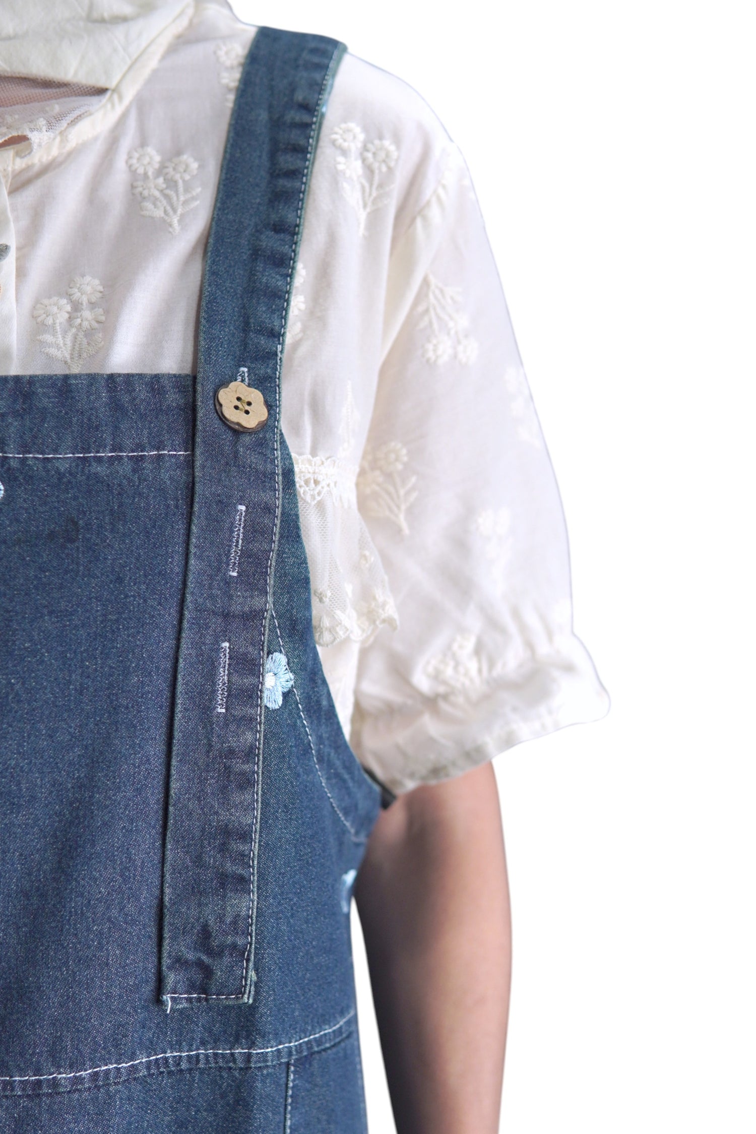 Prim-plan cu bretea reglabilă a rochiei din denim și nasture decorativ în formă de floare.