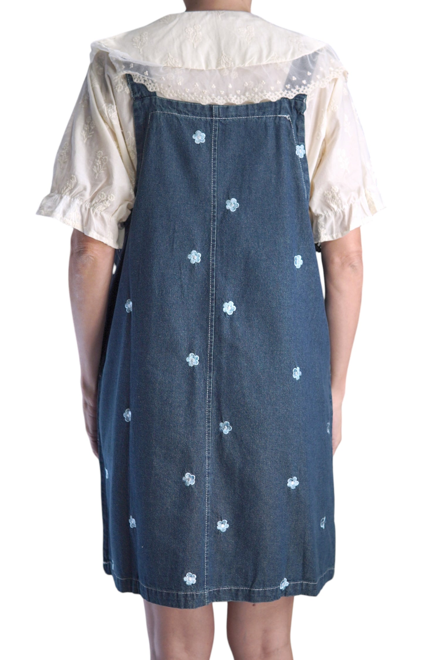 Vedere din spate a rochiei tip salopetă din denim, cu broderii florale delicate.