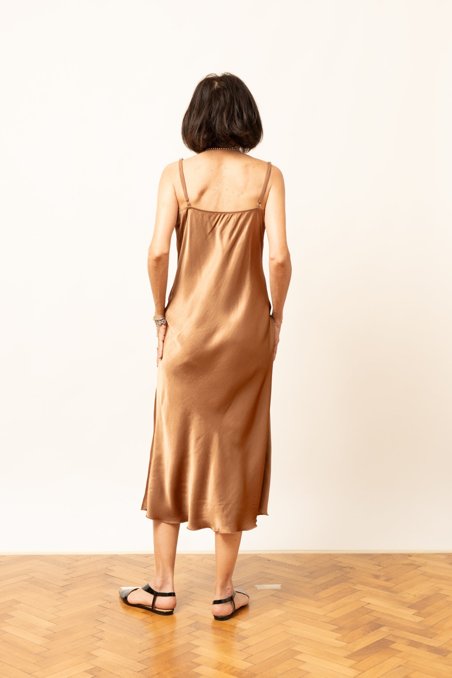 Rochie satinatã midi în nuanță camel, cu bretele subțiri și decolteu drapat, vedere din spate.