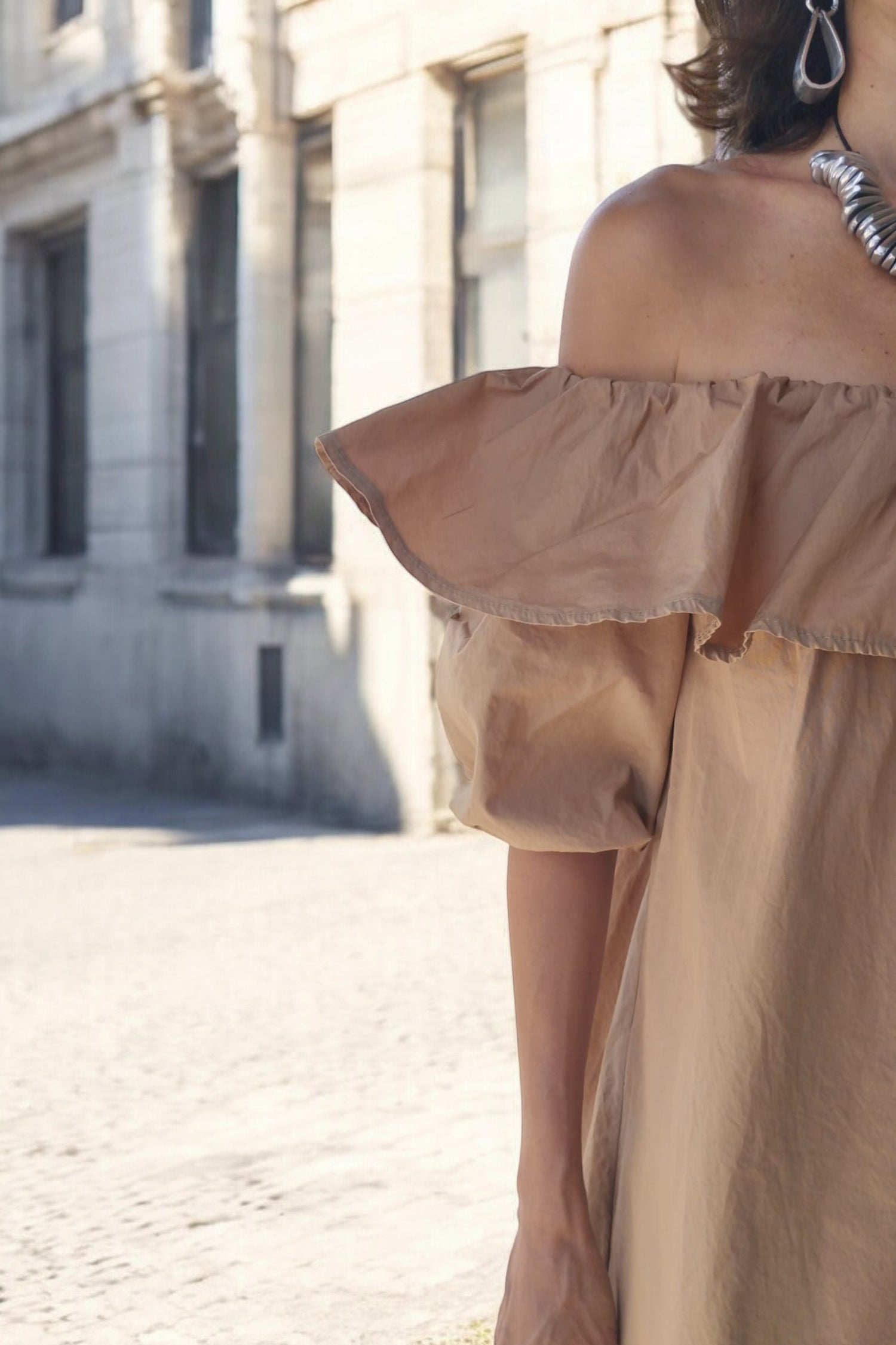 Rochie scurtă bej, cu decolteu elastic tip bardot și volan lat, detaliu elegant.