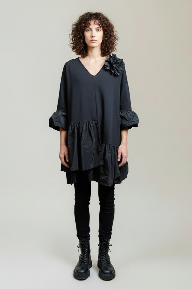 Rochie scurtă neagră cu umeri căzuți, decolteu în V și volane asimetrice, purtată cu bocanci.