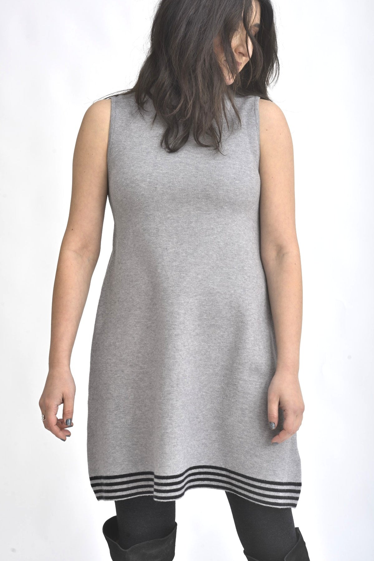 Rochie tricotată gri, fără mâneci, cu croială evazată și tiv decorativ în dungi contrast, purtată cu colanți negri.