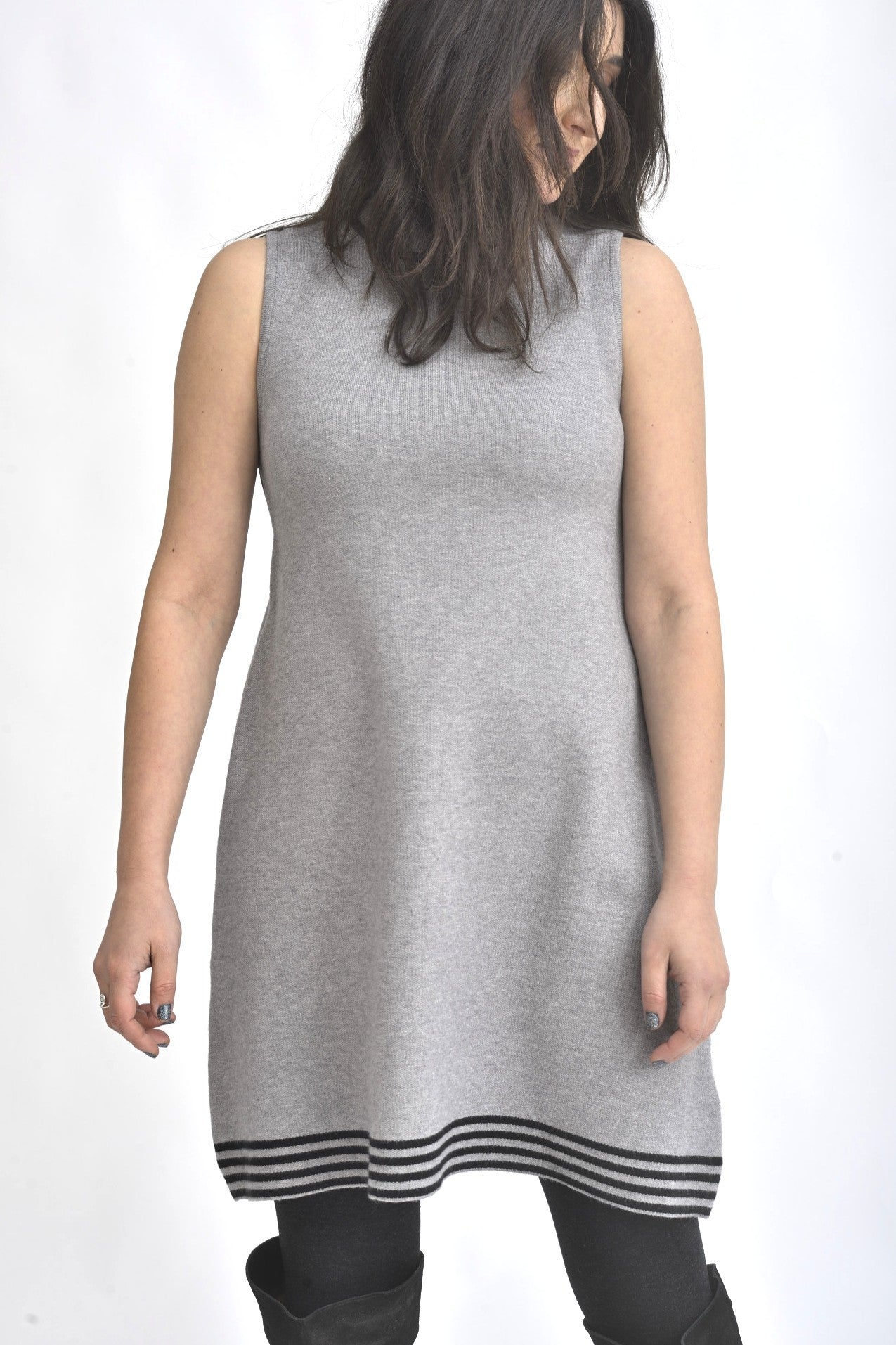 Rochie tricotată gri, fără mâneci, cu croială evazată și tiv decorativ în dungi contrast, purtată cu colanți negri.