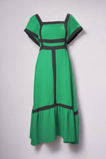 Rochie verde intens cu croială evazată și decupaje negre geometrice, cu decolteu pătrat și volan la bază.

