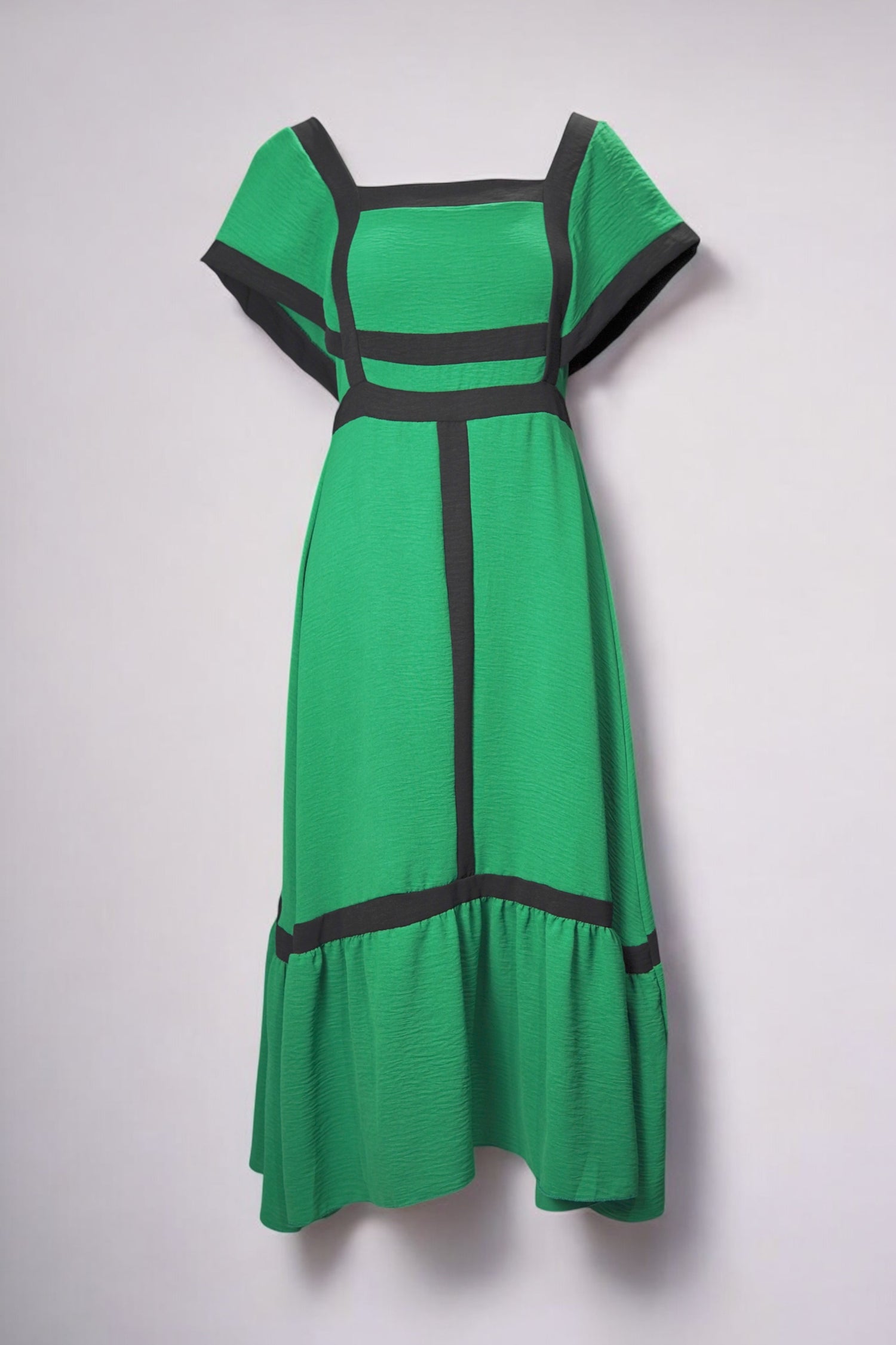 Rochie verde intens cu croială evazată și decupaje negre geometrice, cu decolteu pătrat și volan la bază.

