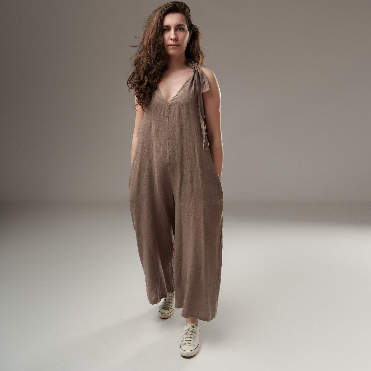 Salopetă culotte din in bej‑taupe, lejeră, cu bretele ajustabile și buzunare ascunse pe cusătură, prezentare frontală pe model.