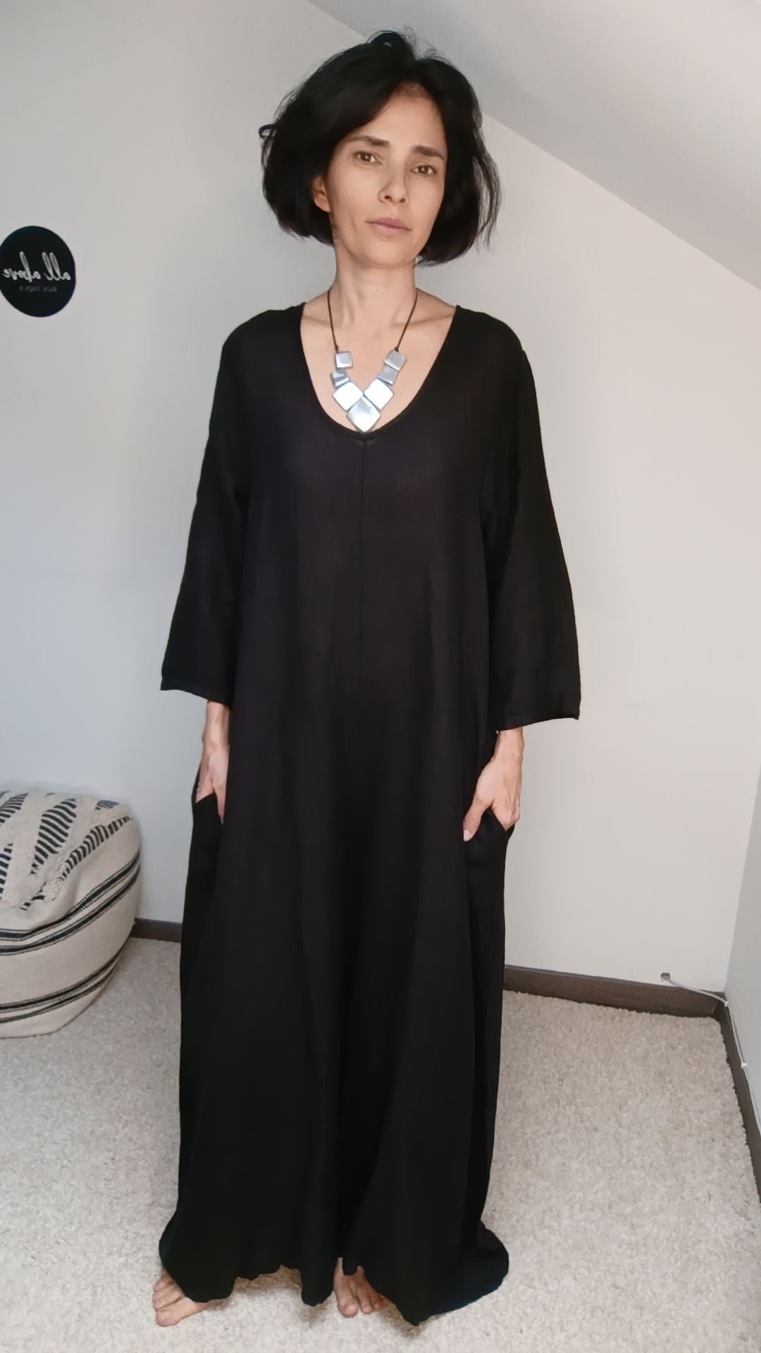 Salopetă din in negru purtată de model cu colier argintiu, croială amplă și buzunare adânci.