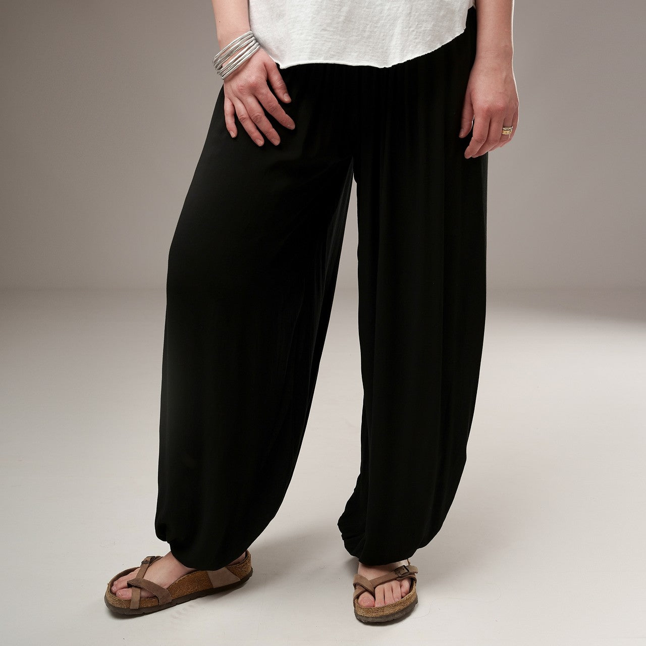 Detaliu de material și croială al unui pantalon tip șalvari negru din bumbac, cu talie elastică drapată și picior prins în partea de jos.