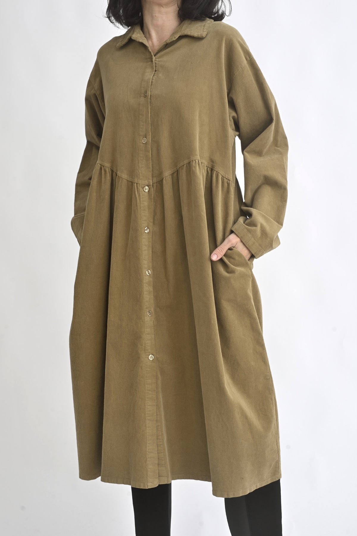 Sarafan cămașă din reiat maro, cu nasturi pe toată lungimea și croială lejeră, purtat peste colanți.