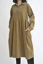 Sarafan cămașă din reiat maro, cu nasturi pe toată lungimea și croială lejeră, purtat peste colanți.