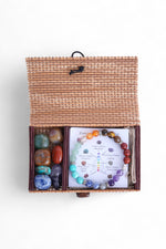 Set cu 7 cristale naturale și brățară elastică, prezentate într-o cutie împletită, alături de cristalieră ilustrată.