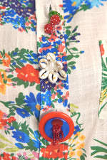 Zoom pe nasturii decorativi în formă de floare, cireșe și cerc colorat de pe cămașă.