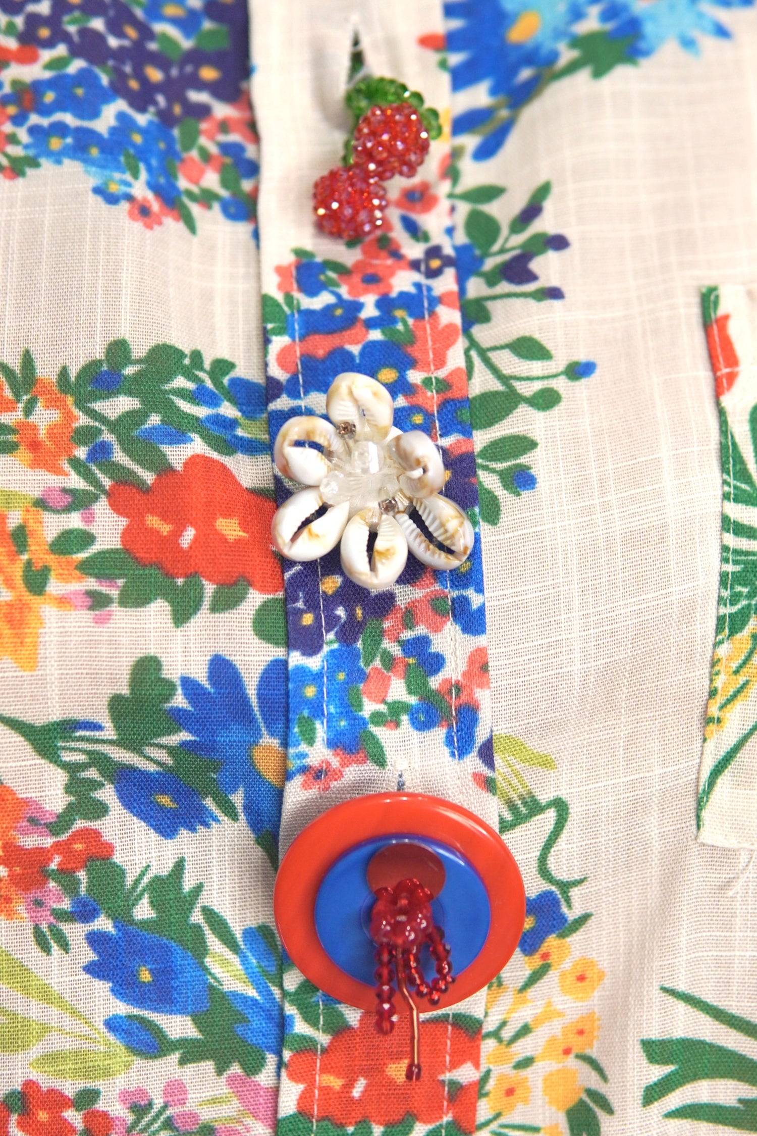 Zoom pe nasturii decorativi în formă de floare, cireșe și cerc colorat de pe cămașă.