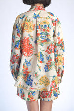 Vedere din spate a cămășii lejere și pantalonilor scurți, imprimeu floral pe fundal crem.