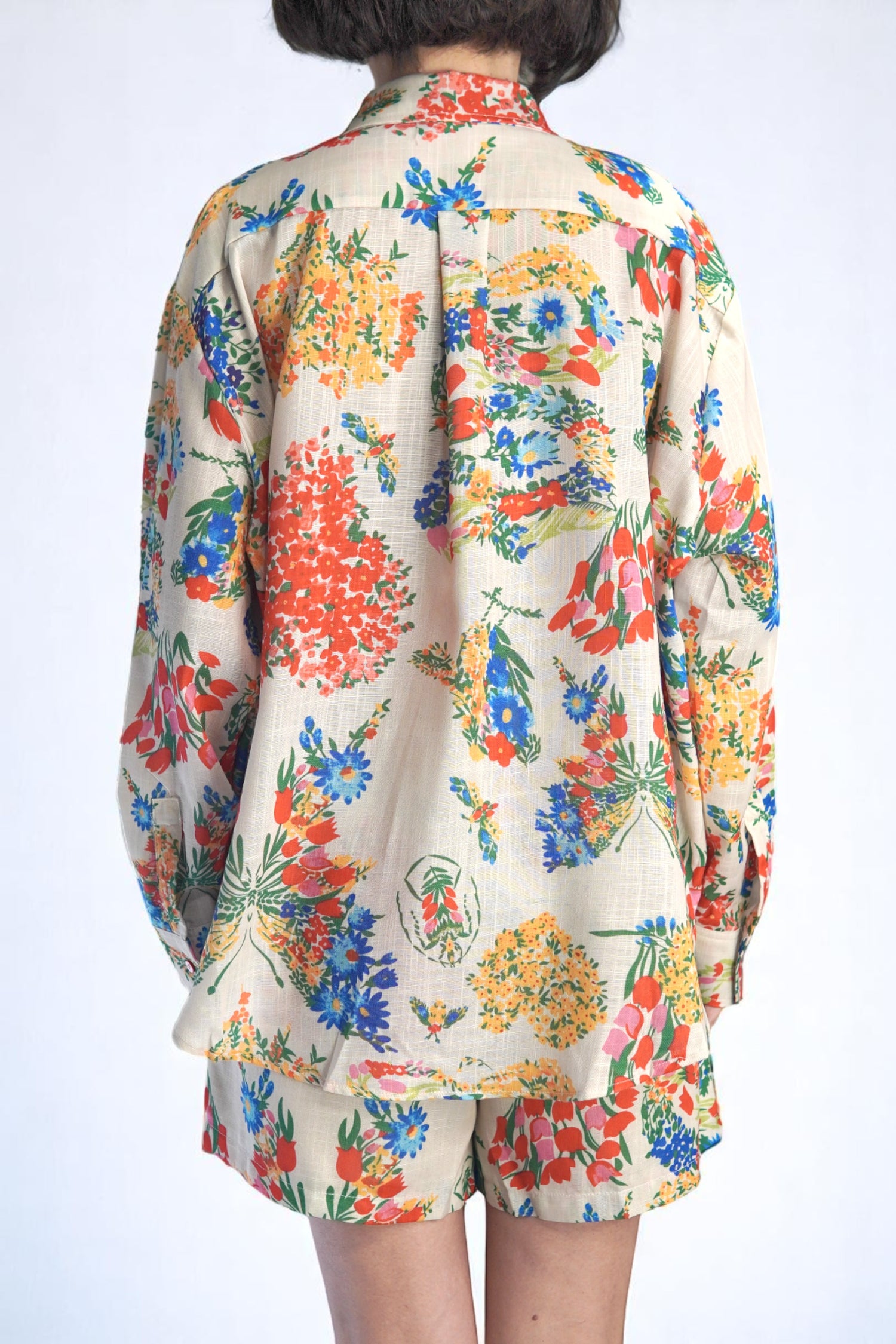 Vedere din spate a cămășii lejere și pantalonilor scurți, imprimeu floral pe fundal crem.