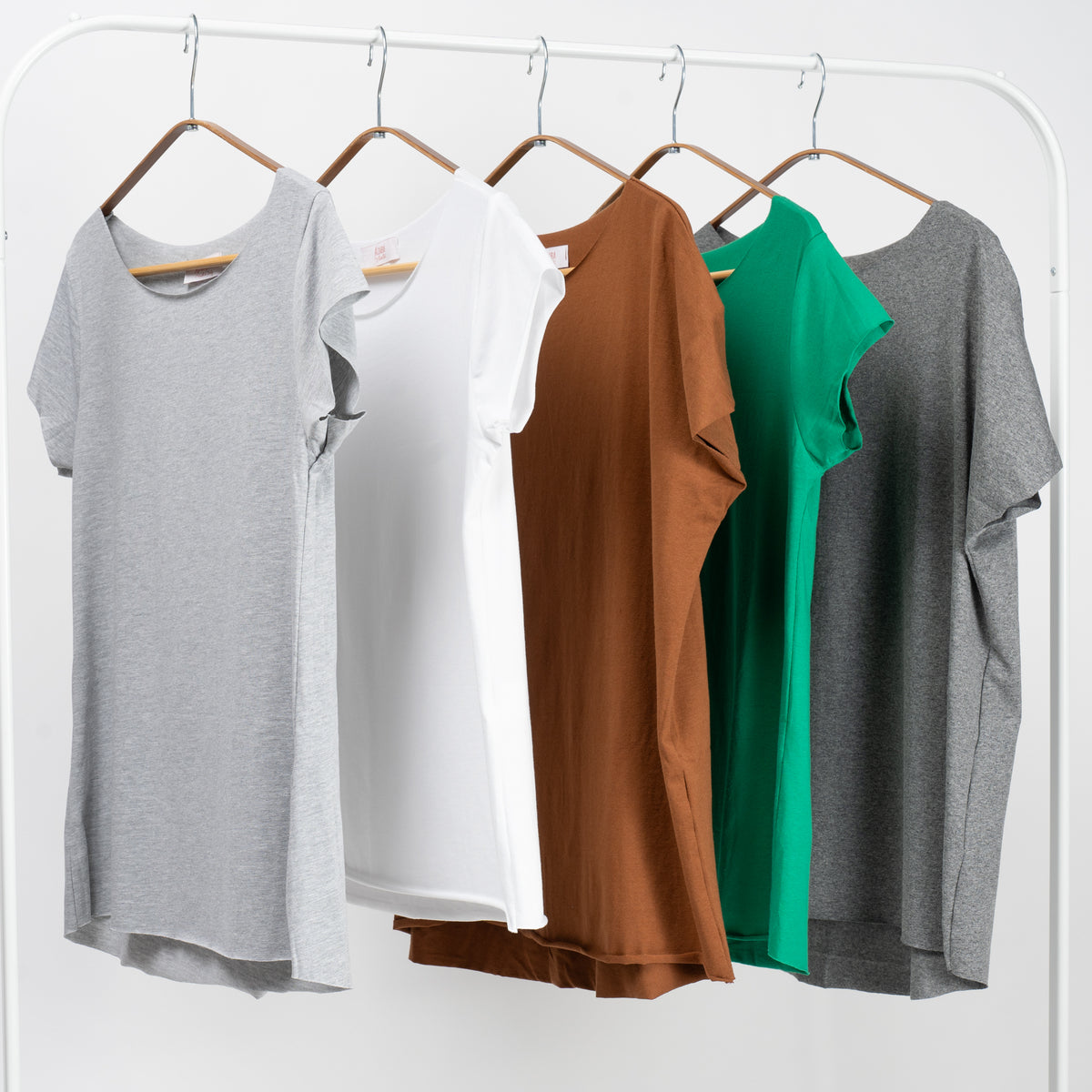  Set de cinci tricouri basic colorate – gri deschis, alb, maro, verde și gri închis – aranjate pe umerașe.

