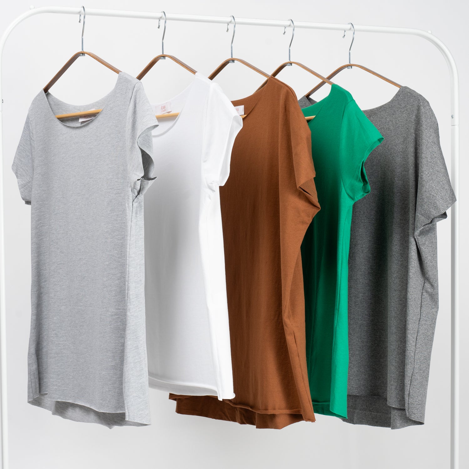  Set de cinci tricouri basic colorate – gri deschis, alb, maro, verde și gri închis – aranjate pe umerașe.

