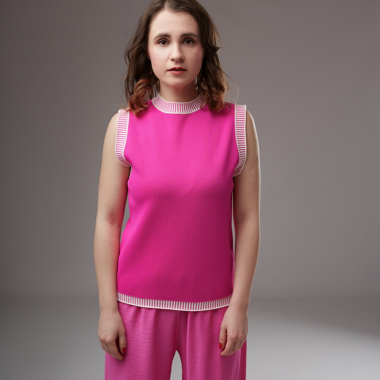 Top tricotat fără mâneci, culoare fucsia intens, cu margini albe în dungi și croială dreaptă, purtat cu pantaloni roz

